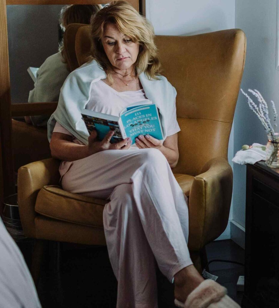 A person sitting in comfortable chair reading a book with smartphone placed on a distant table, representing intentional 
digital boundaries