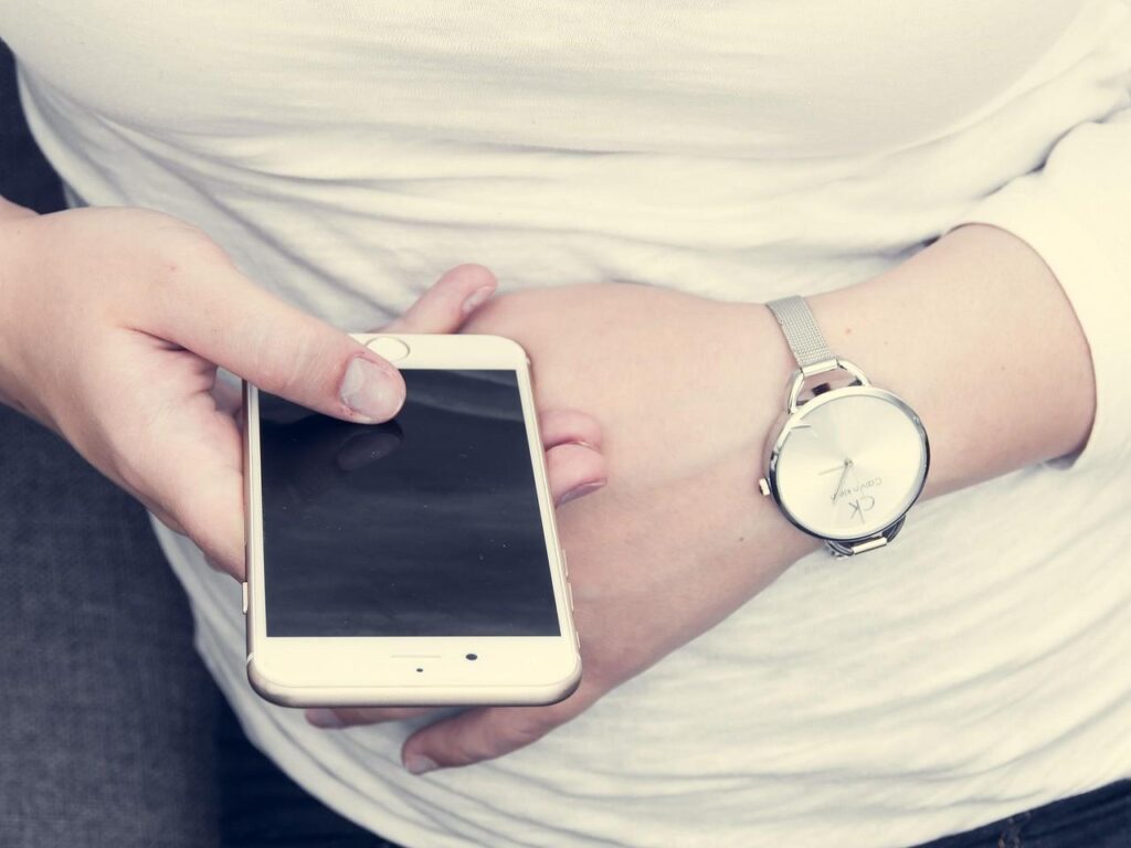 A person lying in bed using smartphone at night with alarm clock showing late hour, representing circadian disruption from blue light