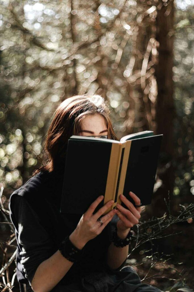 Woman reading a physical book while sitting under a tree during a digital detox retreat in nature