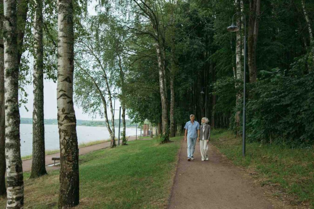 An older woman walking with a friend along a seaside trail, smiling and engaged in conversation, showing walking as social and accessible at any age