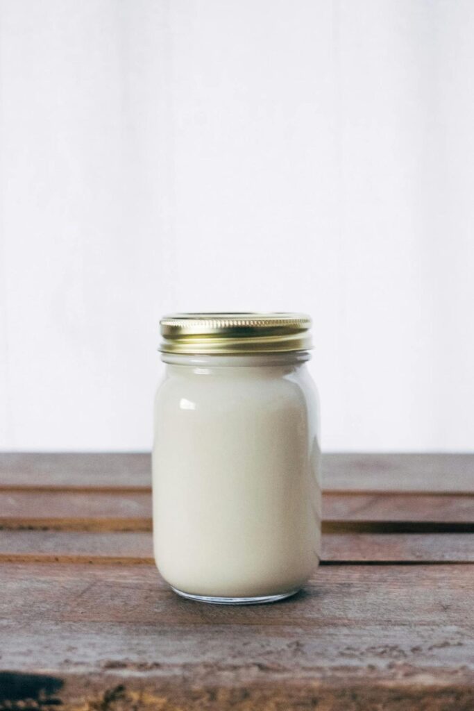 Glass jar filled with solid, creamy white beef tallow placed on rustic wooden kitchen counter with cooking utensils