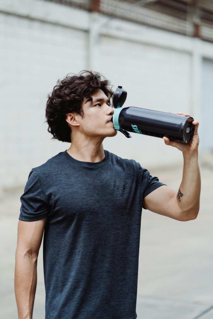 Athlete drinking from water bottle after outdoor workout in hot weather, representing electrolyte replenishment after physical activity