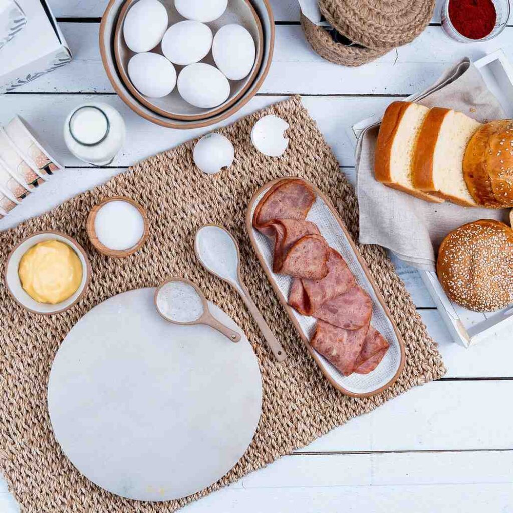 Rustic wooden table displaying traditional whole foods including butter in a dish, farm fresh eggs, glass bottle of milk, crusty bread, and garden vegetables