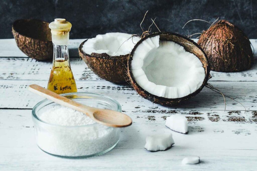 Wooden board with butter, bottle of extra virgin olive oil, glass jar of coconut oil, and piece of bread, representing traditional cooking fats