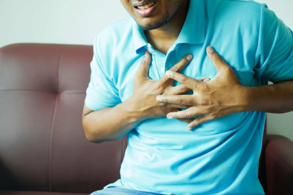  A young person sitting on a city bench, hand on chest with concerned expression, representing the rise of heart issues in younger populations, heart attacks in young people
