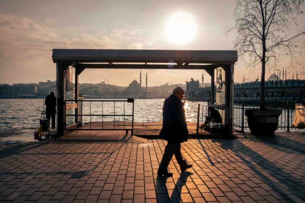 A silhouette of a person walking on a waterfront path during golden hour, representing walking as a time for reflection and peace