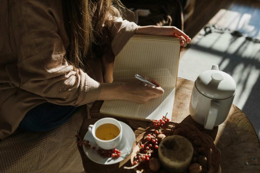 Person writing in a journal at a desk with a cup of tea and warm lamplight, representing self-reflection and coping with anxiety living with anxiety personal story 2026
