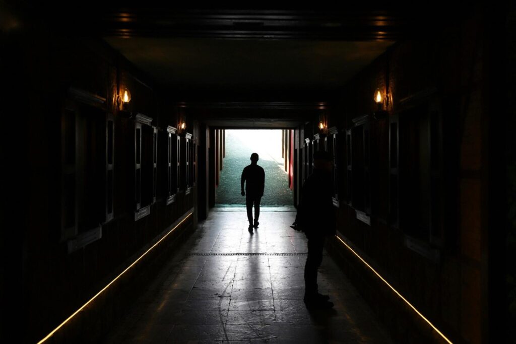  Silhouette of person walking away from dark shadowy figure toward bright open door, representing breaking free from trauma bond. Trauma bonding 2026
