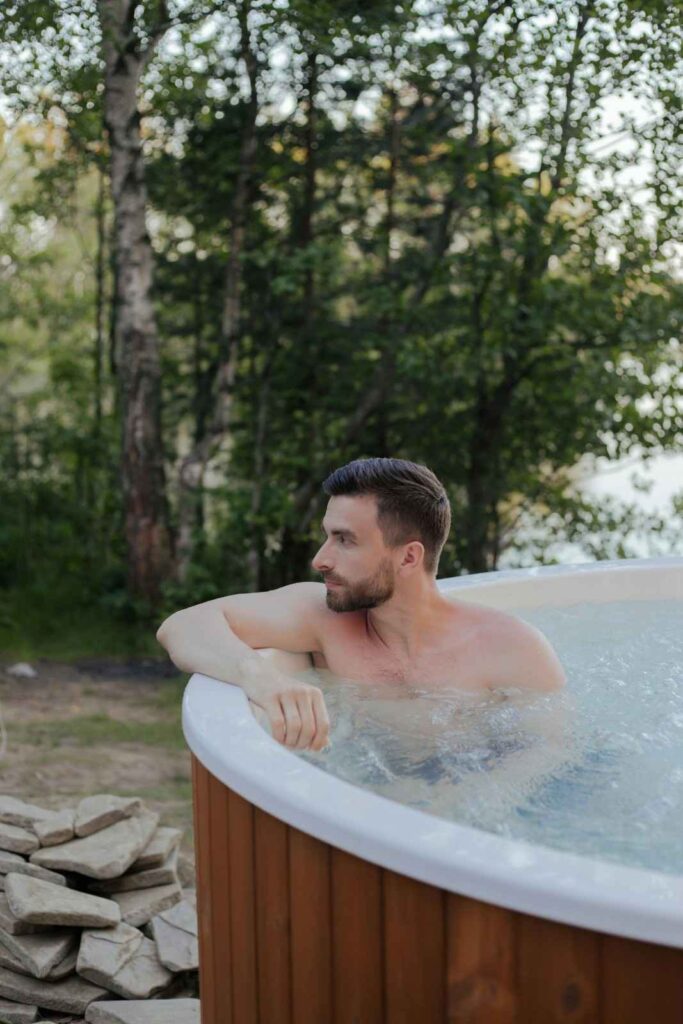  Person sitting calmly in an outdoor ice bath surrounded by trees, representing cold exposure therapy for recovery and resilience
