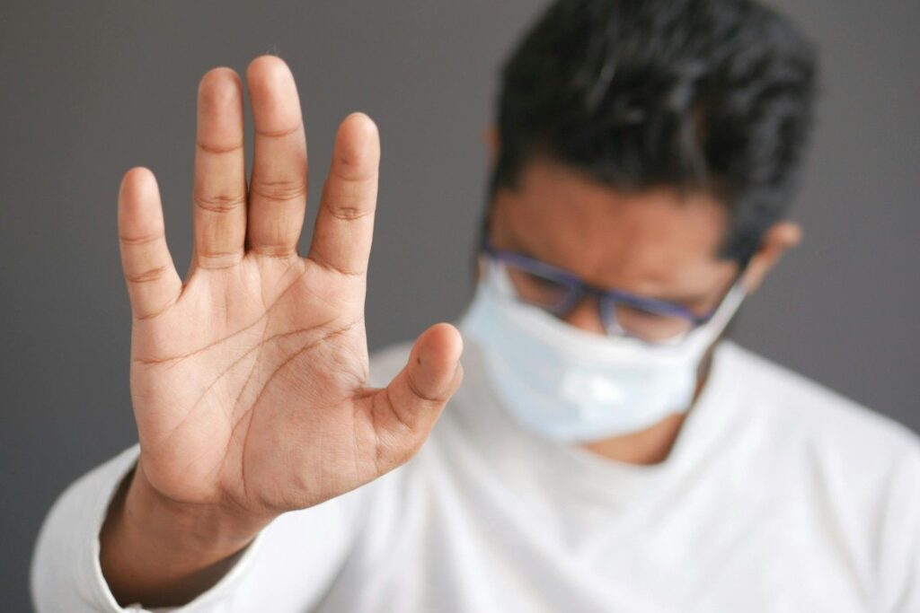 A person standing firmly with hand raised in stop gesture while crowd walks past, representing setting boundaries
